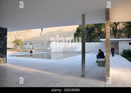 Reflecting pool in geometric building with man seated on stone bench nearby as woman walks towards exit Stock Photo