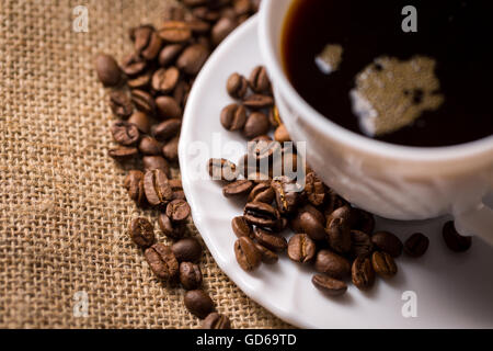 White cup of coffee with saucer and coffeebeans on linen material, closeup, cutted, view from above. Stock Photo