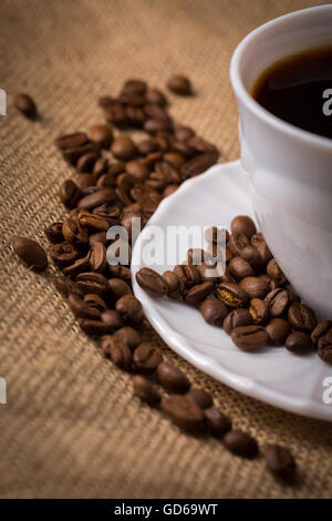 White cup of coffee with saucer and coffeebeans on linen material. Stock Photo