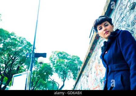 A retro styled girl standing against a graffiti sprayed wall in a urban environment. Stock Photo