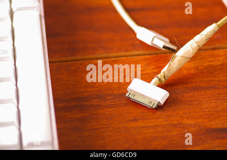 Broken usb mobile charger cable lying on wooden surface, masking tape used to fix wire Stock Photo