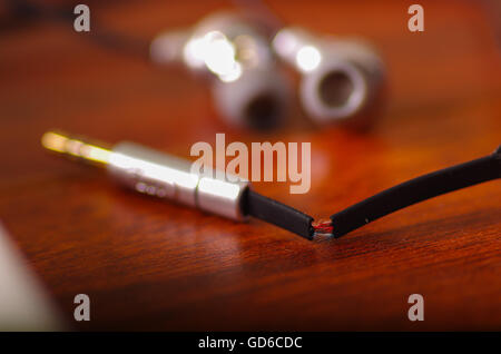 Broken audio headphones cable lying on wooden surface, part of internal wire exposed through cracked plastic Stock Photo