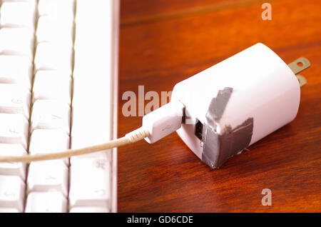 Broken usb mobile charger cable and block lying on wooden surface, silver gaffa tape used for temporary fix Stock Photo