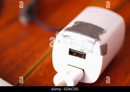 Broken usb mobile charger cable and block lying on wooden surface, silver gaffa tape used for temporary fix Stock Photo