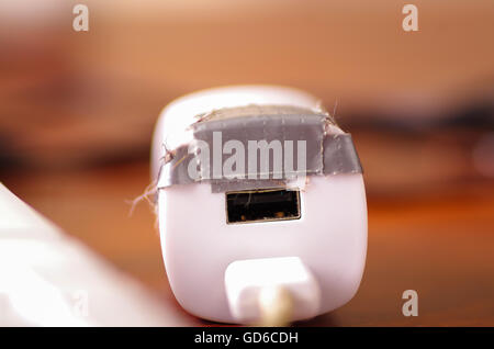 Broken usb mobile charger cable and block lying on wooden surface, silver gaffa tape used for temporary fix Stock Photo