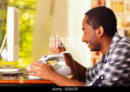 Man standing by desk repairing iron machine using screwdriver, window with garden background Stock Photo