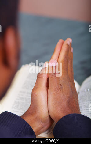 Man folding hands praying with open bible lying in front, seen from behind models head, religion concept Stock Photo
