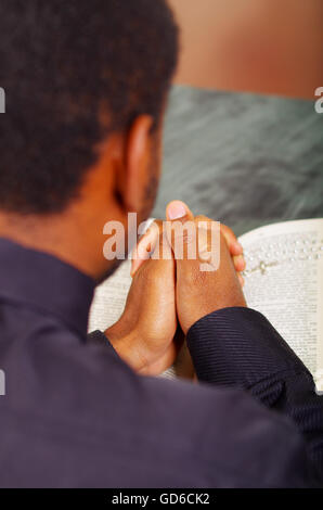 Man folding hands praying with open bible lying in front, seen from behind models head, religion concept Stock Photo