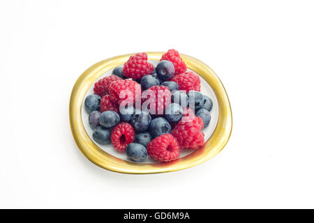 Group of raspberries and bilberries  placed on a golden dish with white isolated background. Stock Photo
