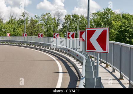 white arrows on red road signs, indicating a protracted left turn Stock Photo