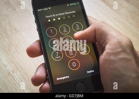 Apple iPhone5s held in one hand showing its screen with numpad for entering the passcode Stock Photo