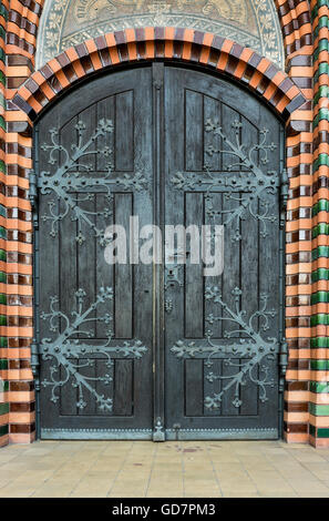 Massive wooden church door with a handle forged with an iron grip settled into a brick wall at the church. Breclav. South Moravi Stock Photo