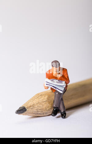 Concept image of a male figure looking through a newspaper sat on a pencil looking at a crossword puzzle or looking for a job Stock Photo
