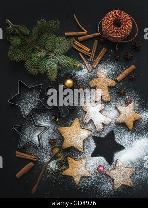 Cooked Christmas holiday traditional gingerbread cookies with sugar powder, cinnamon sticks and fir branches on black background Stock Photo