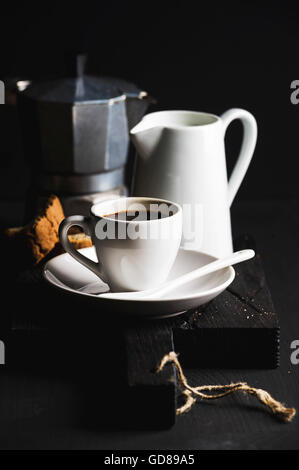 Italian coffee breakfat set. Cup of hot espresso, creamer with milk, cantucci and moka pot and cookies on dark rustic wooden boa Stock Photo