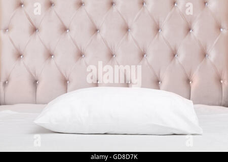 Luxury empty bedroom interior fragment, soft pink headboard, white pillow lays on wide empty bed Stock Photo