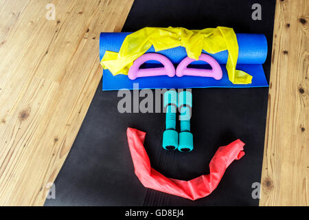 Resistance bands and hand weights on yoga mats set out in a smiley face pattern on wooden floor background