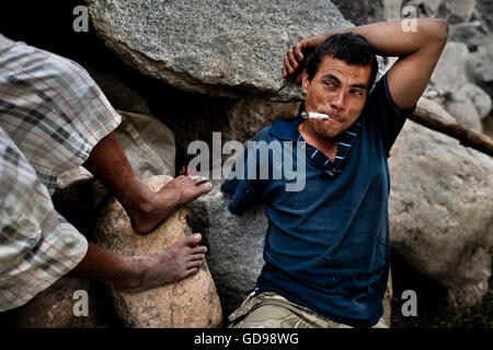 A young Honduran immigrant, having his arm amputated by a train, smokes marijuana on the bank of Suchiate river in Guatemala. Stock Photo