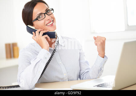 Hispanic female professional with glasses talking on the phone and smiling in the office Stock Photo