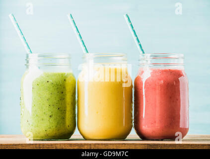 Freshly blended fruit smoothies of various colors and tastes in glass jars with blue straws. Green, yellow, red. Turquoise blue Stock Photo