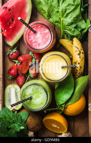 Fresh blended smoothies in glass jars with straws on wooden baclground served with watermelon, kiwi, orange, banana, strawberry, Stock Photo