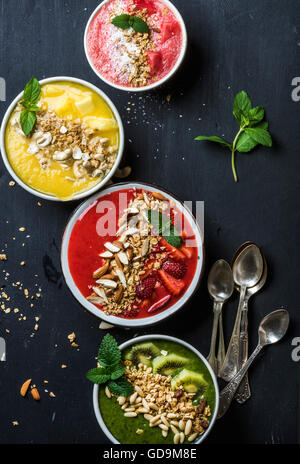 Healthy summer breakfast concept. Colorful fruit smoothie bowls with nuts and oat granola served with mint leaves and silver spo Stock Photo