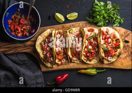 Shrimp tacos with homemade salsa sauce, limes and parsley on wooden board over dark background. Top view. Mexican cuisine Stock Photo