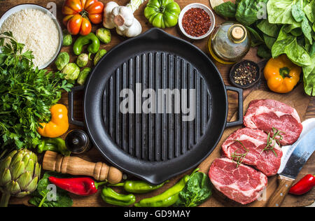 Ingredients for cooking healthy meat dinner. Raw uncooked beef steaks with vegetables, rice, spices and olive oil over wooden ba Stock Photo