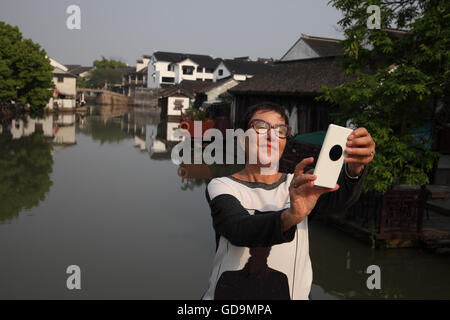A 70 year old senior citizen Israeli woman, a tourist, is using her smartphone to take a selfie over Tongli's the main canal. Stock Photo