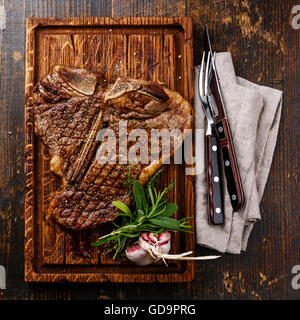 Grilled T-Bone Steak with fork and knife on serving board on wooden background Stock Photo