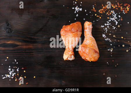 Raw Marinated chicken meat legs for BBQ with seasoning salt and pepper over dark wooden background. Top view with copy space. Stock Photo