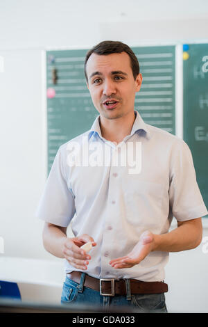 Young teacher near chalkboard in school classroom talking to class Stock Photo