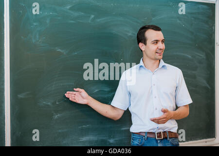 Young male teacher pointing at blank blackboard and talking Stock Photo
