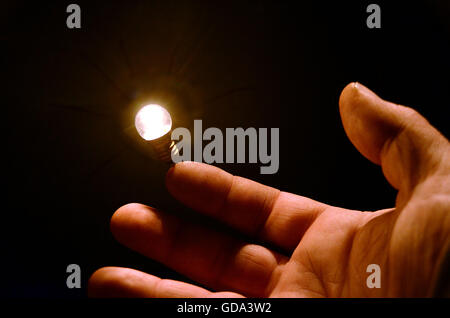 A light bulb seems to balance on a human finger. Stock Photo
