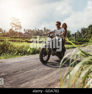 Outdoor shot of couple on motorbike driving through country road. Man and woman riding motorcycle on a countryside road. Stock Photo