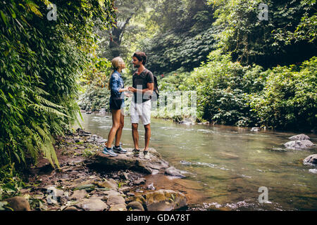 Outdoor shot of loving couple standing by a mountain stream in the rainforest. Hiker couple standing by stream in woods. Stock Photo