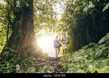 Young man and woman hiking in tropical jungle. Couple of hikers walking along forest trail. Stock Photo