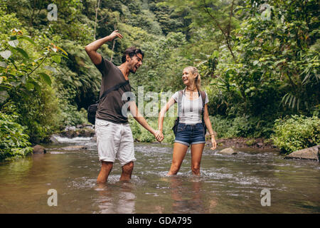 Excited young couple in mountain stream. Young man and woman standing in river holding hands and enjoying. Stock Photo