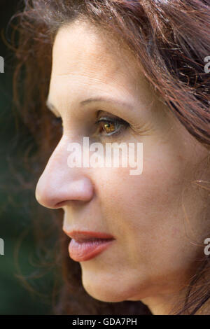 profile portrait of mature woman with long wavy  reddish brown hair, red lipstick and dreaming look Stock Photo