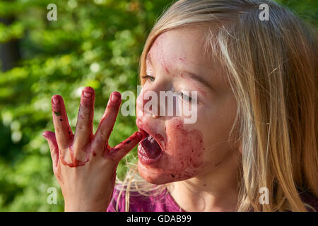 Girl licking tinged blueberries from fingers. Summer family fun. Stock Photo