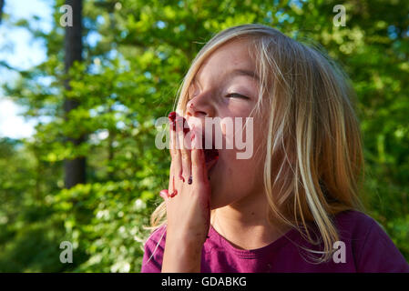 Girl licking tinged blueberries from fingers. Summer family fun. Stock Photo