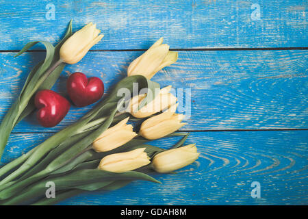 Yellow tulips and two red decorative stone hearts on a blue wooden rustic table with copy space, retro tones Stock Photo