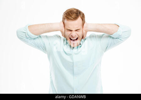 Irritated stressed young man covered ears by hands and shouting over white background Stock Photo
