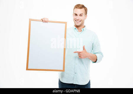 Cheerful young man holding blank white board and pointing on it over white background Stock Photo