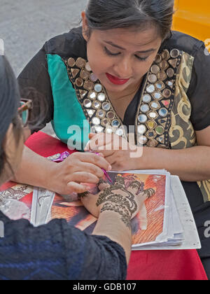 A woman from Bangladesh decorates a woman's hand with henna for the Eid al Fitr festival. In Jackson Heights, Queens, New York. Stock Photo