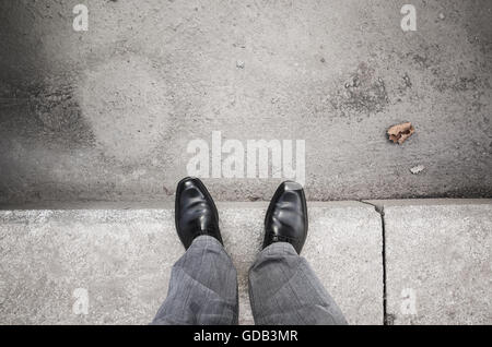 Feet of an urbanite man in black new shining shoes standing on gray curb