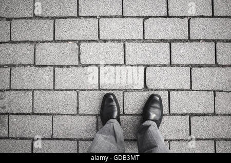 Feet of an urbanite man in black new shining shoes standing on gray cobblestone road