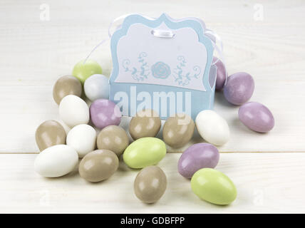 Colored sugared almonds and papery box on white wooden background Stock Photo