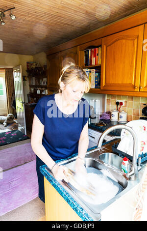 Woman washing up dishes pots cleaning at sink bowl clean cleaner washer soapy water UK England Stock Photo