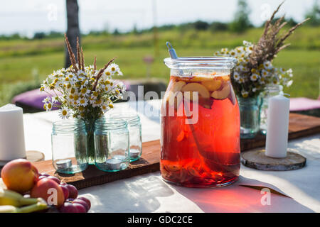 Fresh compote, fruits, candles and flowers on wooden table closeup. Selective focus. Beutiful decoration in boho style. Stock Photo